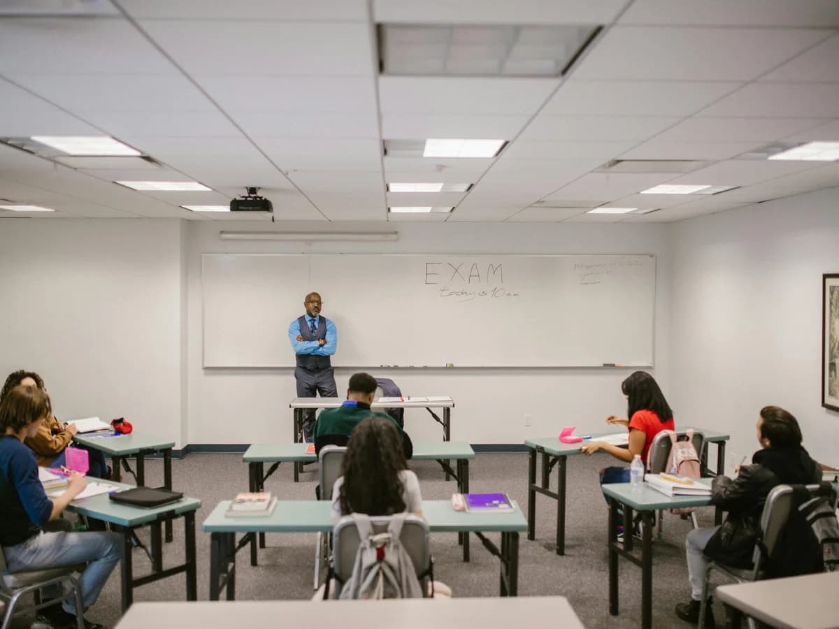 Teacher and students in a classroom with 'EXAM' written on the whiteboard